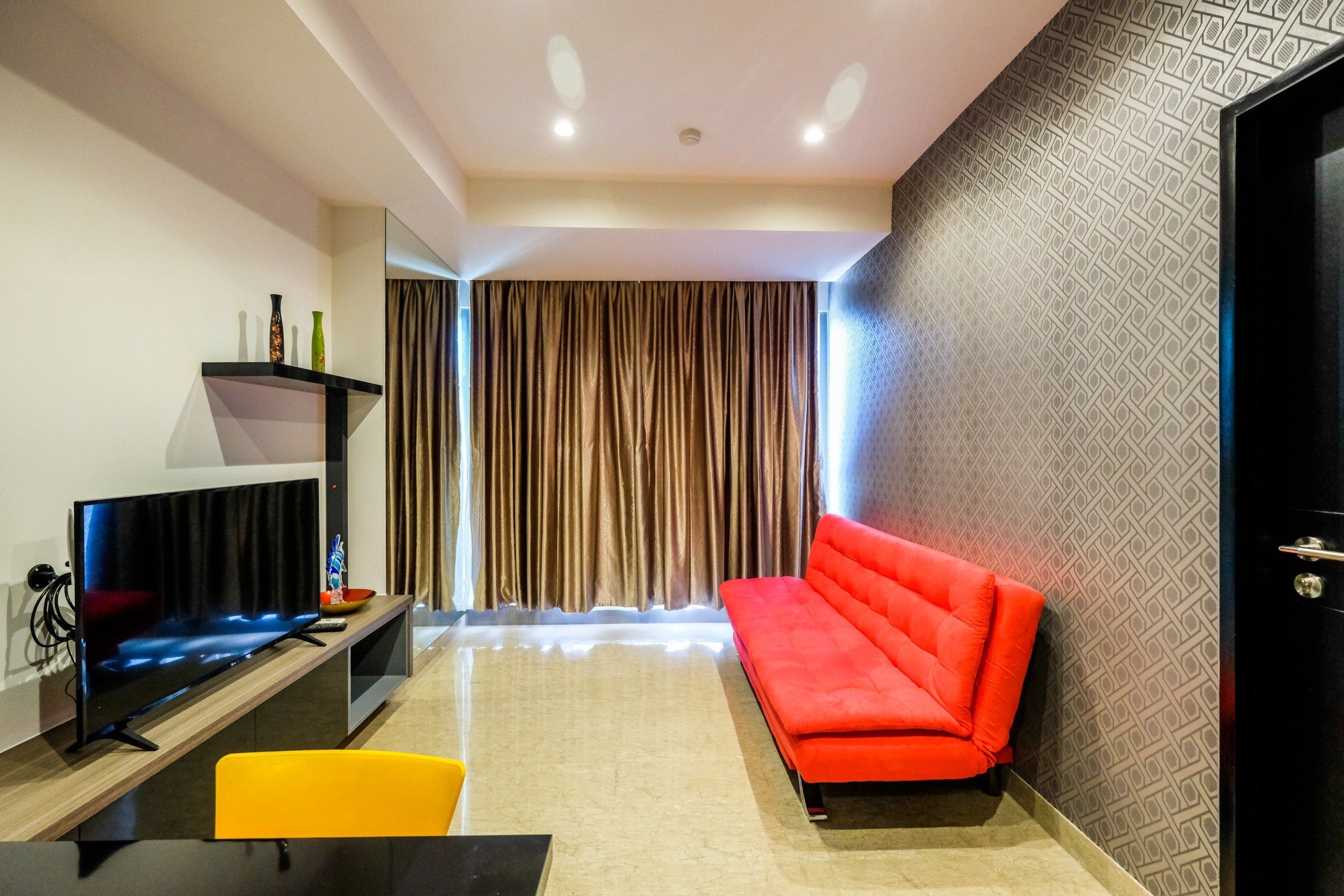 A modern living room with a flat-screen TV, a red sofa, and a yellow chair.