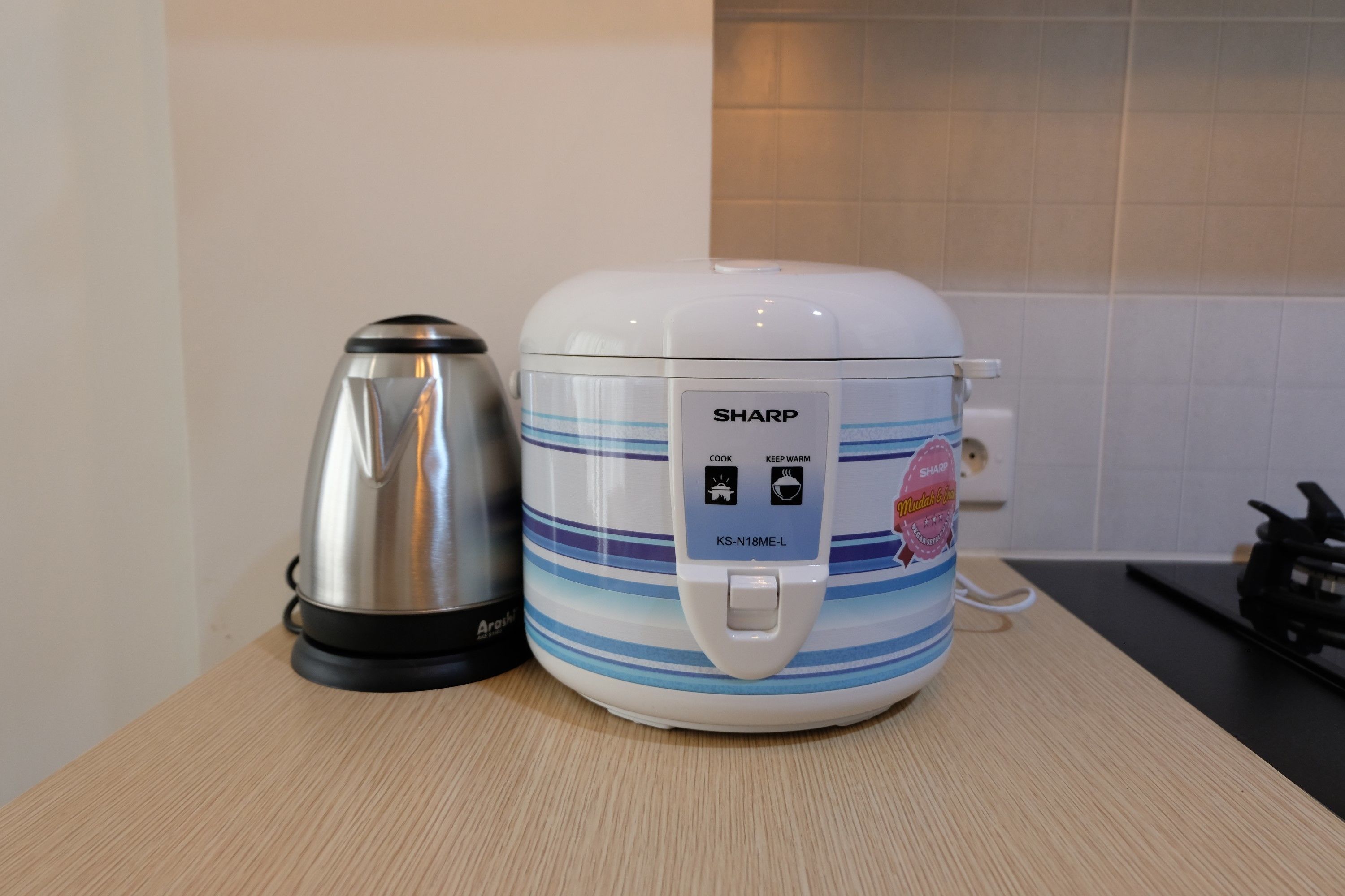A kitchen with a white Sharp rice cooker and a silver electric kettle on a wooden countertop.