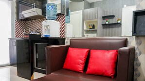 A modern kitchen with a built-in stove, a water dispenser, and a microwave. There is a brown leather sofa with red cushions in the foreground. - Comfy and Clean 2BR Green Pramuka Apartment (Jakarta)