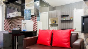 A modern kitchen with a water dispenser, a refrigerator, and a coffee machine. There is a brown leather sofa with red cushions in the foreground. - Comfy and Clean 2BR Green Pramuka Apartment (Jakarta)