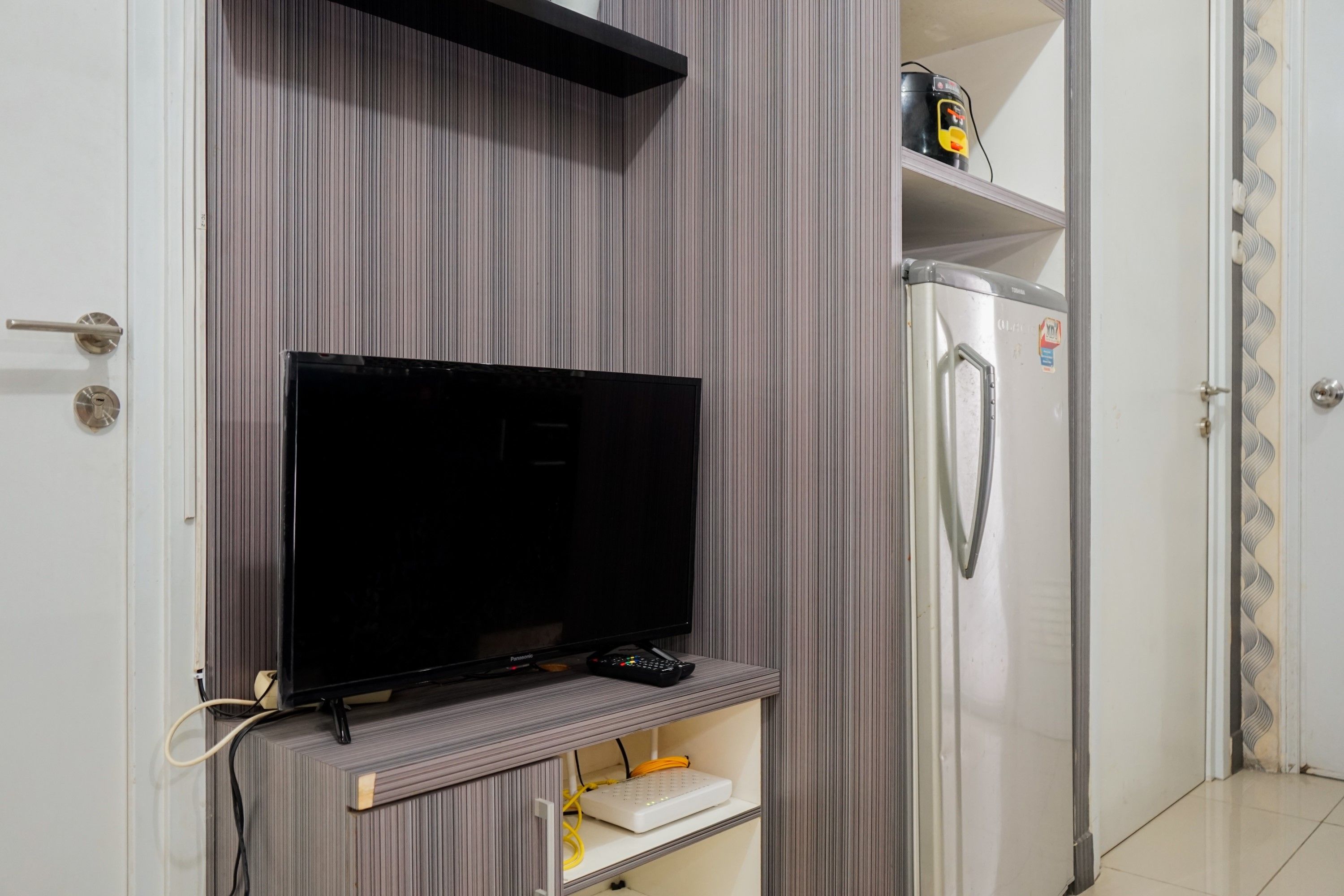 A modern kitchen with a built-in flat-screen TV, a refrigerator, and a shelf with a can of drink.