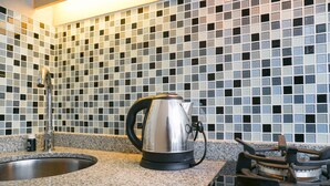 A kitchen with a granite countertop, a stainless steel kettle, a gas stove, and a sink.