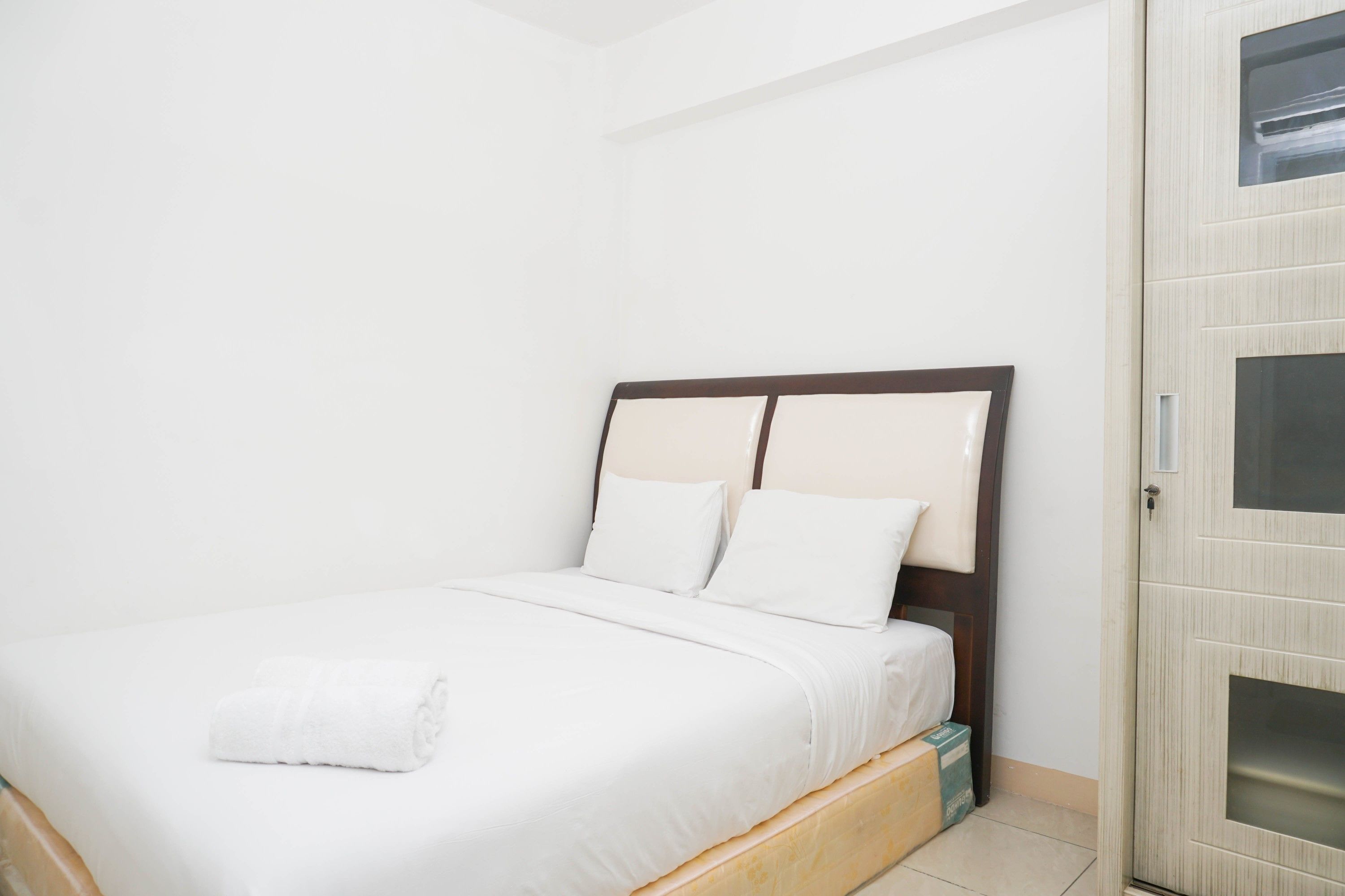 A neatly made bed with white linens and pillows, a wooden headboard, and a small bedside table with a box.