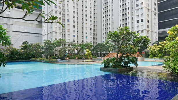 A swimming pool surrounded by greenery and tall residential buildings.