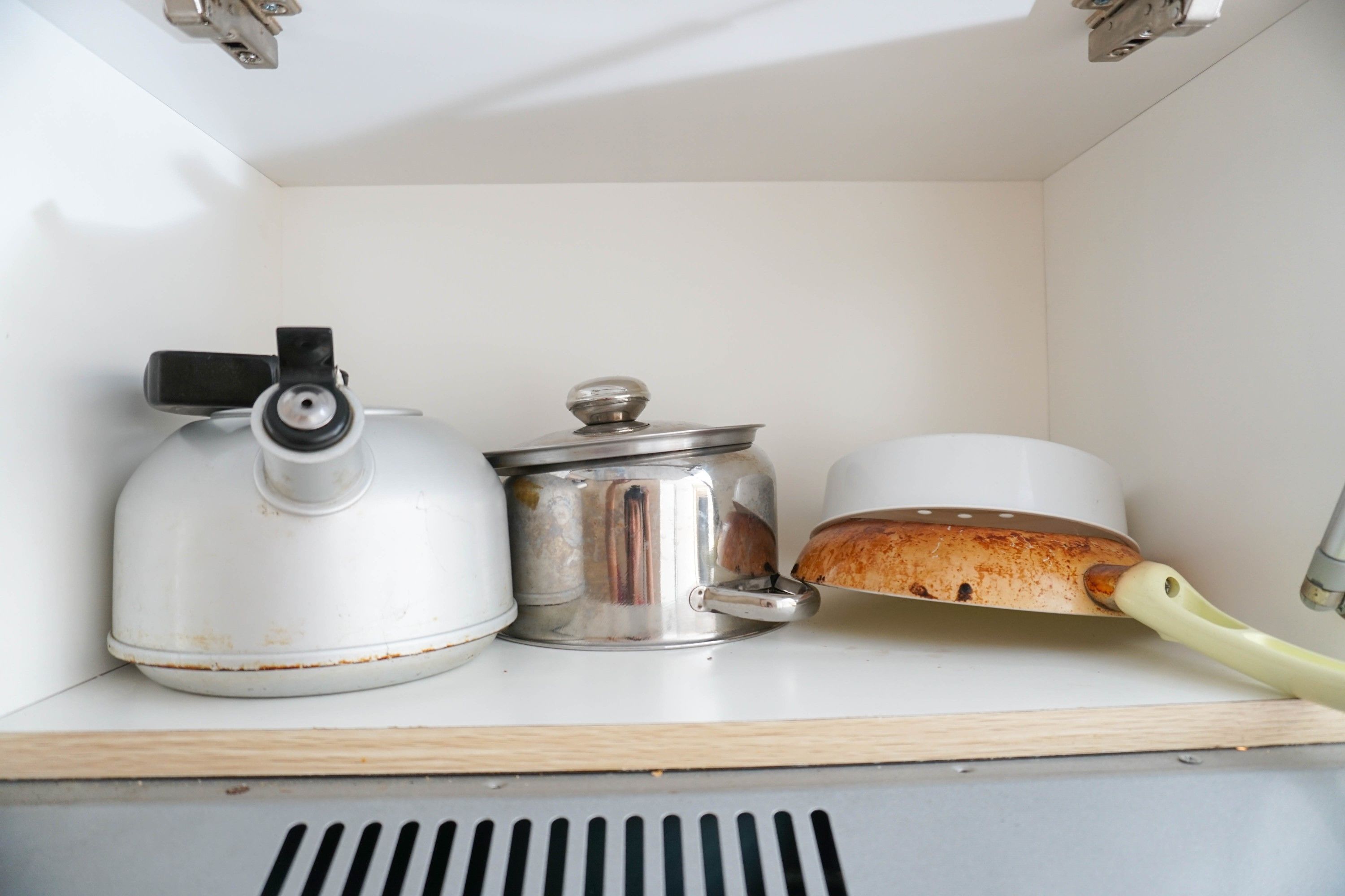 Une étagère de cuisine avec une bouilloire blanche, une casserole en acier inoxydable et une miche de pain.