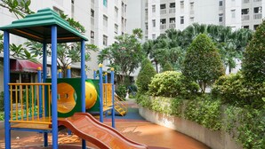 A playground with slides and climbing structures, surrounded by greenery and a building in the background.