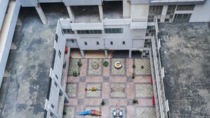 Vista aérea de un patio con un parque infantil, zonas de estar y fachada de edificio.