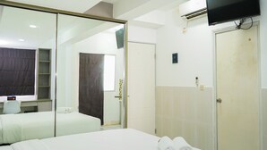Una habitación de hotel con una cama grande, una mesita de noche, un espejo, un televisor montado en la pared y un equipo de aire acondicionado.