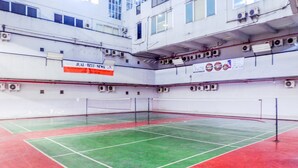 Una cancha de squash con piso verde y rojo, rodeada de paredes con unidades de aire acondicionado y un cartel.