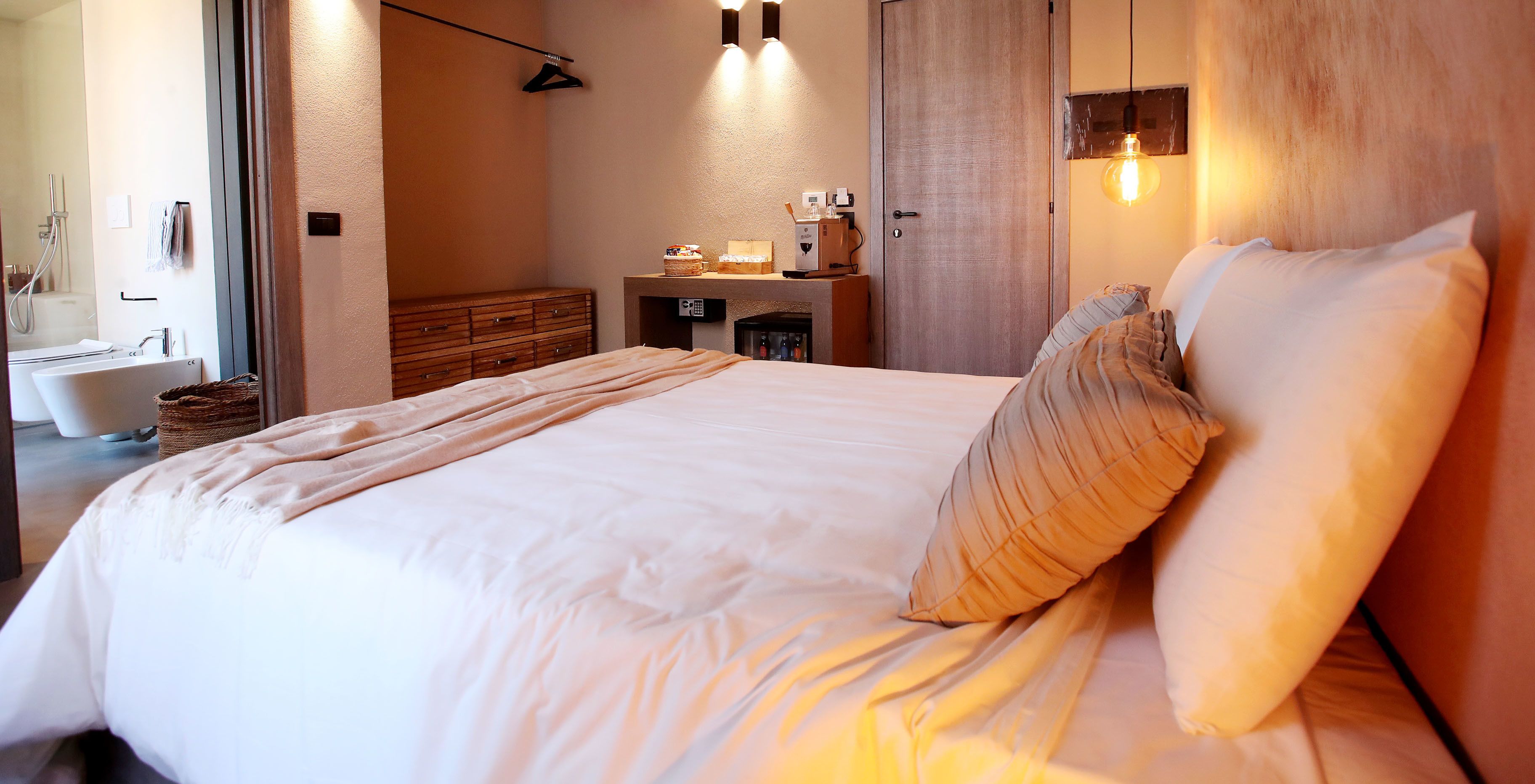 Un dormitorio moderno con una cama grande, un aparador de madera, un tocador con espejo y una pequeña kitchenette.