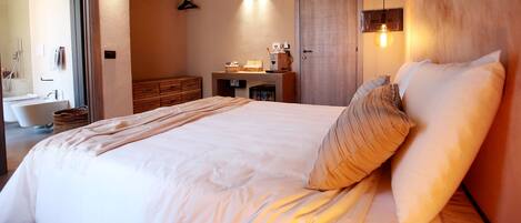 Un dormitorio moderno con una cama grande, un aparador de madera, un tocador con espejo y una pequeña kitchenette.