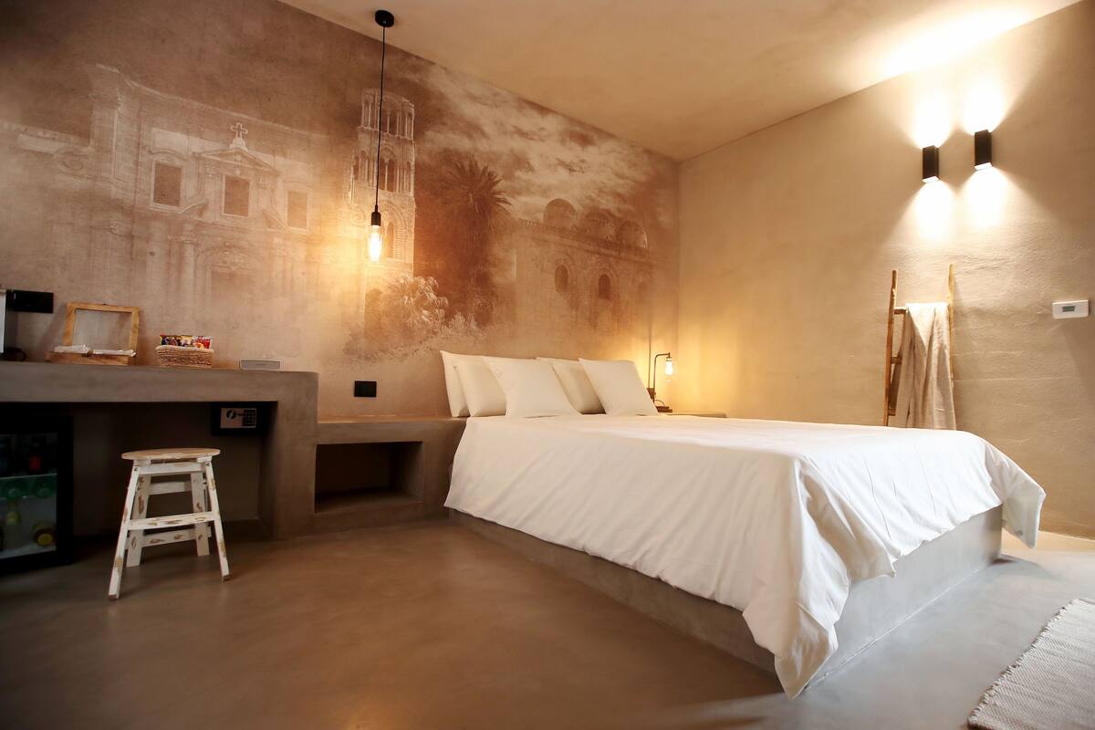 Ein Schlafzimmer mit einem Bett, einem kleinen Hocker, einem Nachttisch und Wandmalerei.