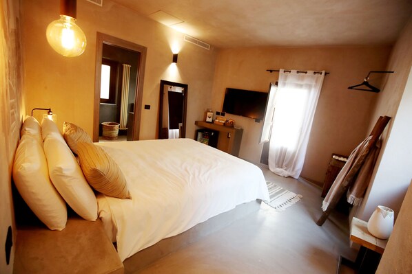 Une chambre à coucher avec un grand lit, des tables de chevet, un téléviseur à écran plat, un miroir et une fenêtre avec des rideaux.