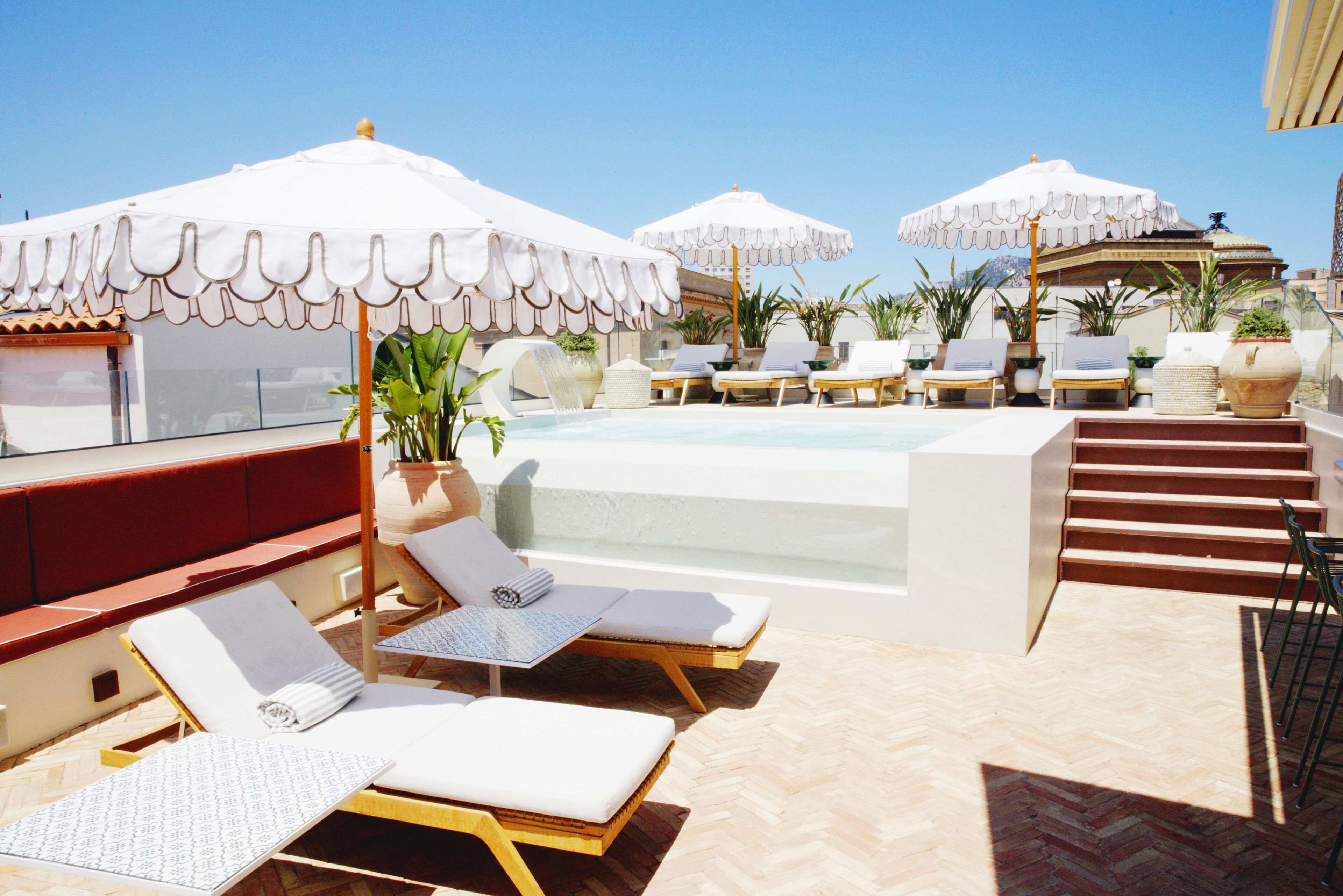 A rooftop pool area with lounge chairs, umbrellas, and a hot tub.
