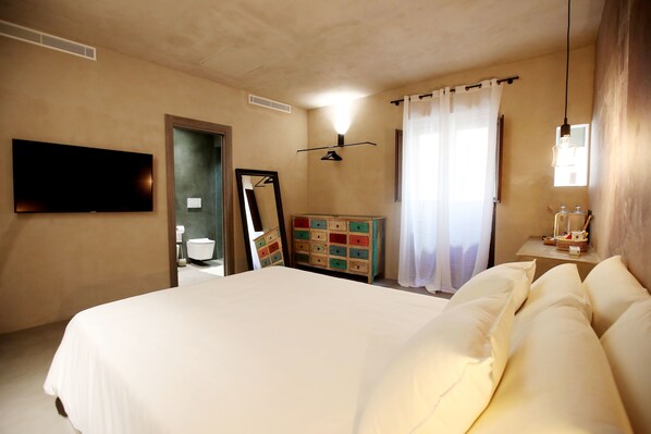 Een hotelkamer met een groot bed, een dressoir, een spiegel, een televisie en een raam met gordijnen.