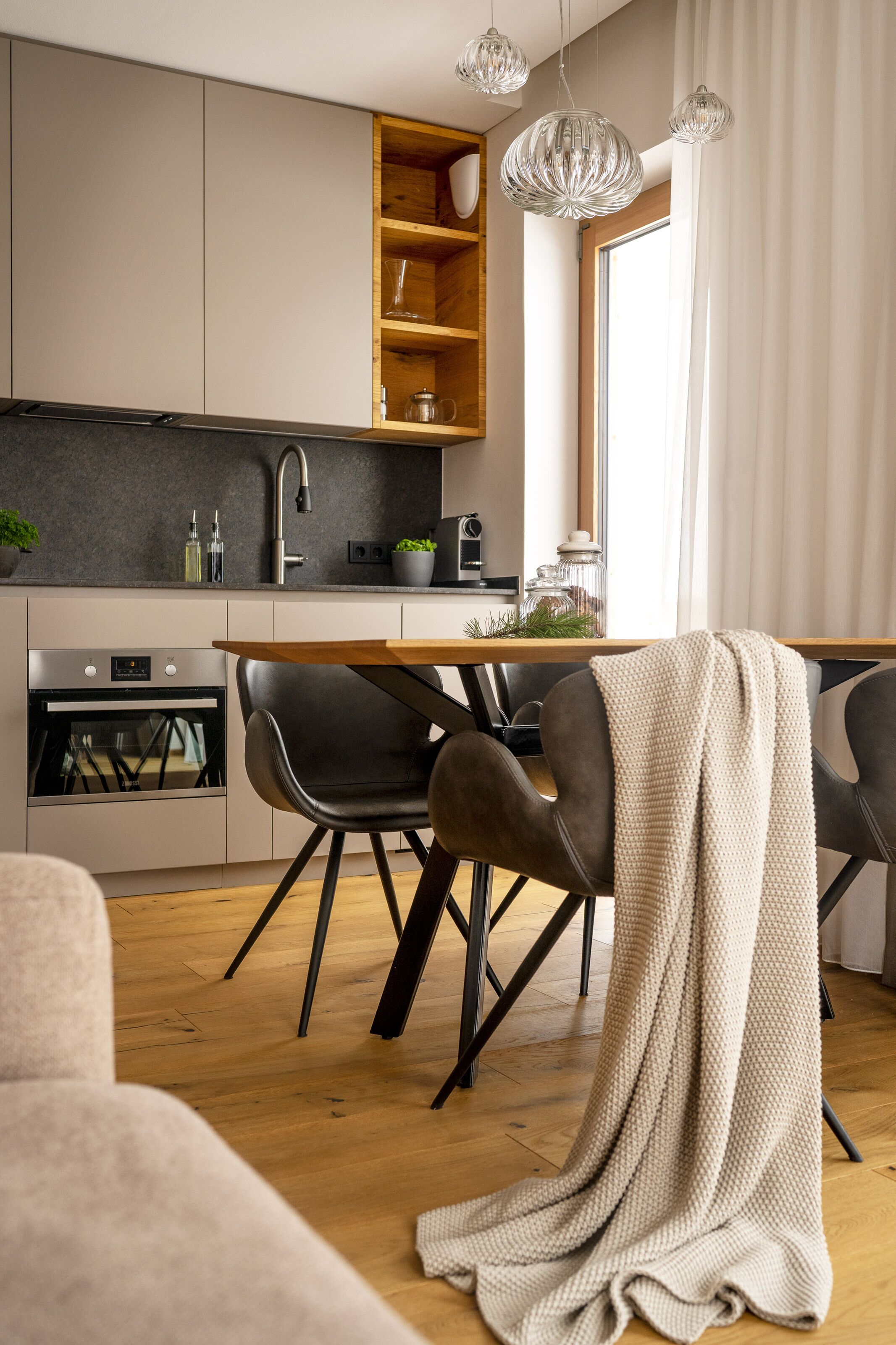 A modern kitchen with a built-in oven, a dining table with chairs, and pendant lights.