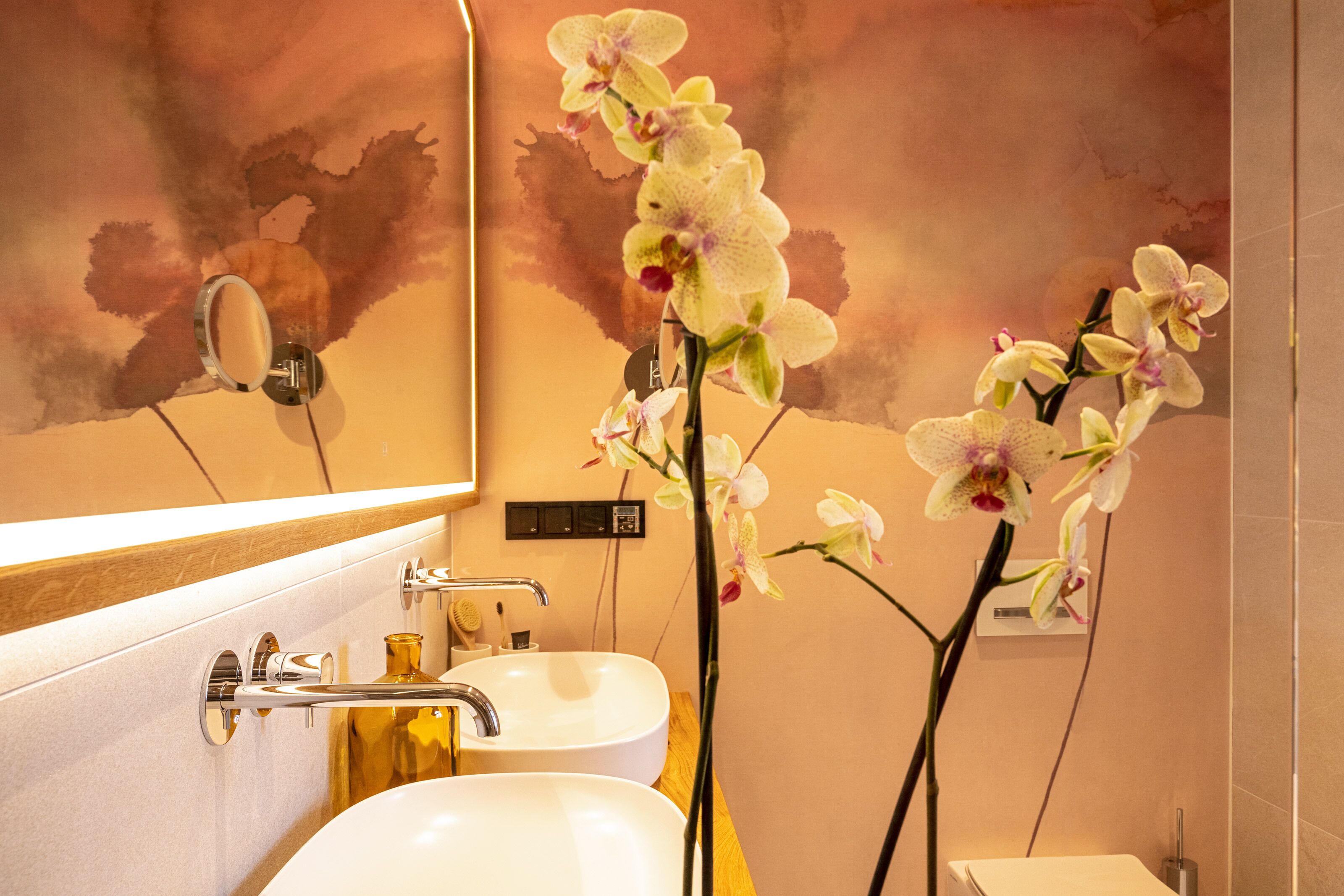 Ein Badezimmer mit zwei Waschbecken, einem Spiegel und Orchideen.