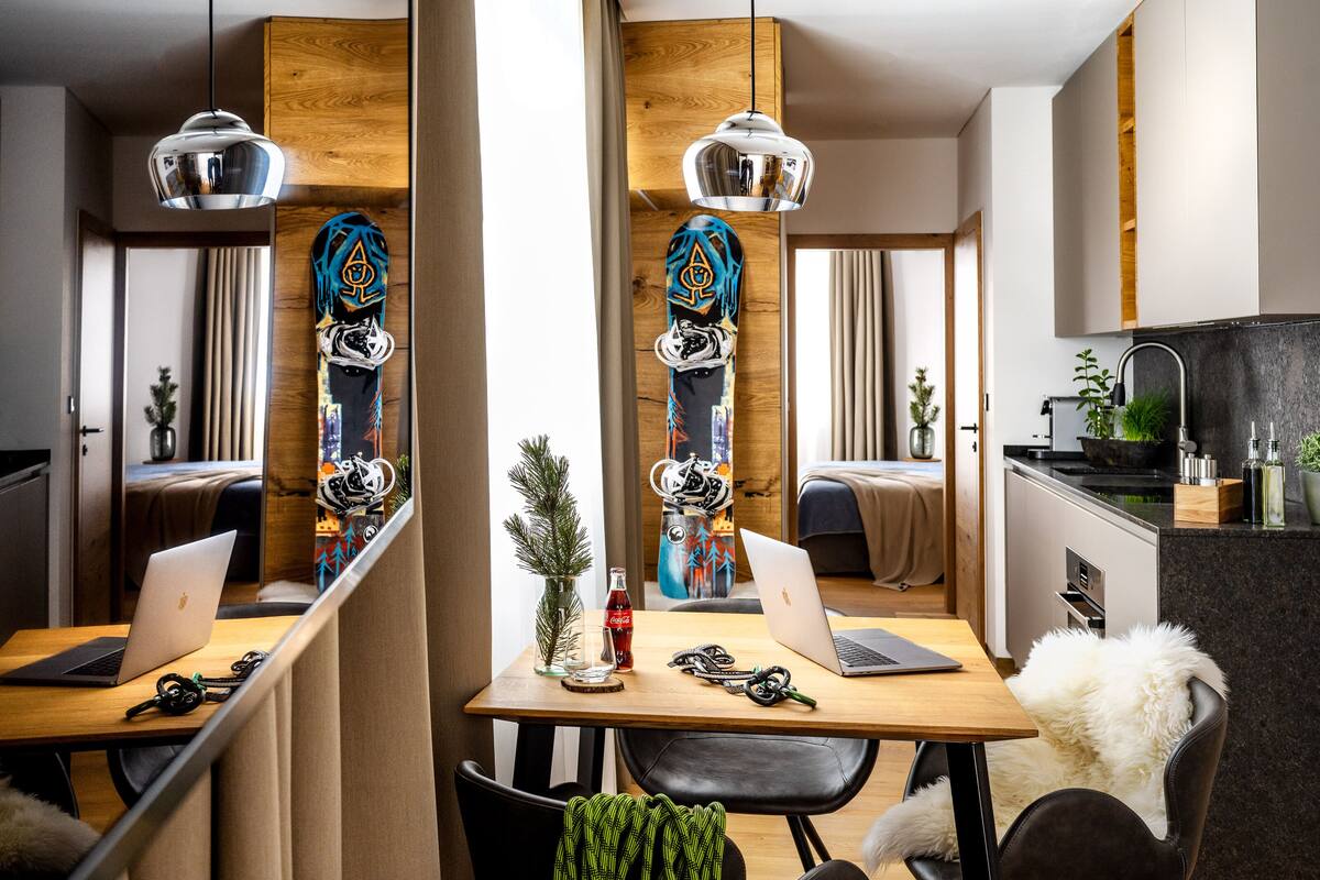 Un comedor moderno con una mesa de madera, dos portátiles, una tabla de snowboard y una planta pequeña.