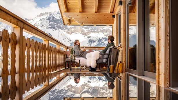 Een houten terras met een glazen vloer die uitzicht geeft op een besneeuwde berg.