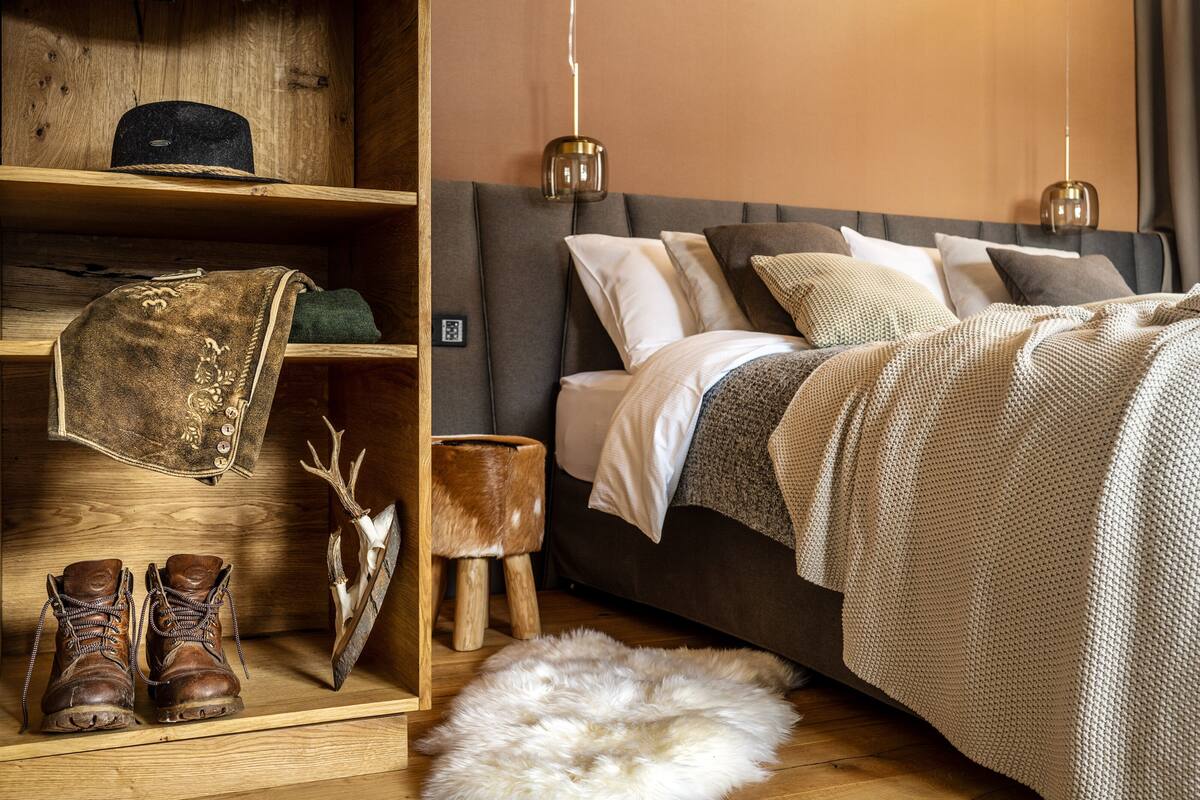 Un dormitorio con una cama, estanterías de madera, botas, una alfombra de piel y un cuerno de ciervo.