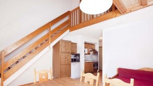 A wooden staircase leading to a loft bedroom with a red bed and a dining area with a wooden table and chairs. - VVF Résidence Plagne 1800 Paradiski (La Plagne-Tarentaise)