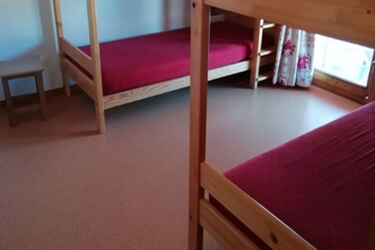 Habitación con literas de madera, un taburete pequeño de madera y una ventana con cortinas.