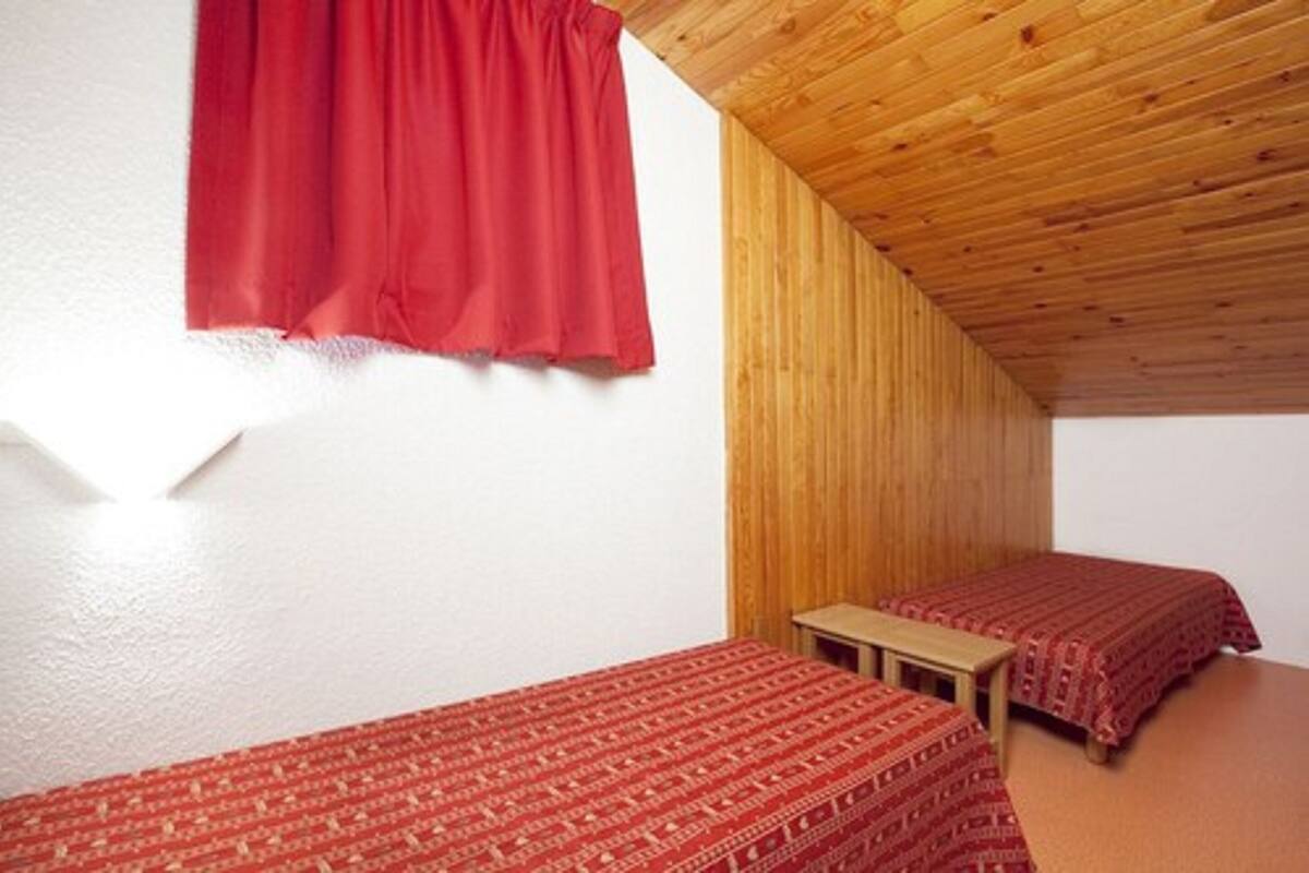 Una habitación pequeña y acogedora con dos camas individuales, techo de madera y cortina roja.