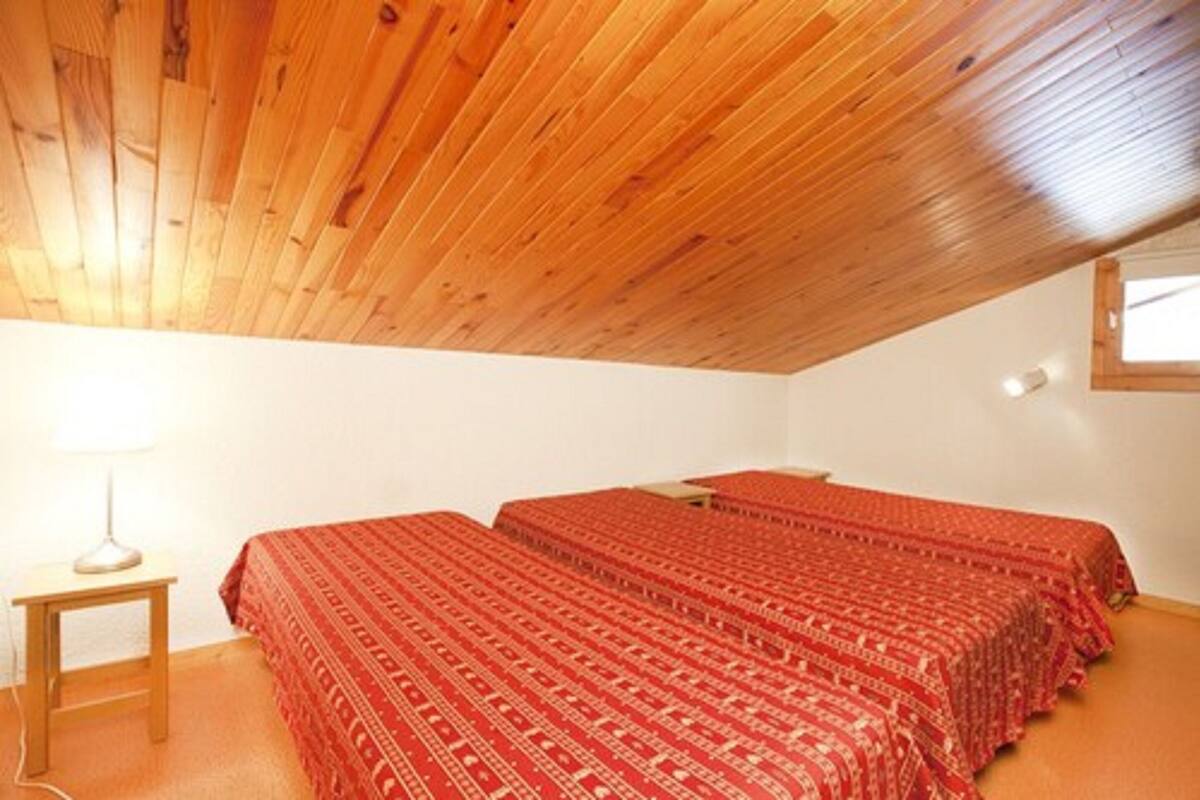 Una habitación pequeña con dos camas, techo de madera, una mesita de noche y una ventana.