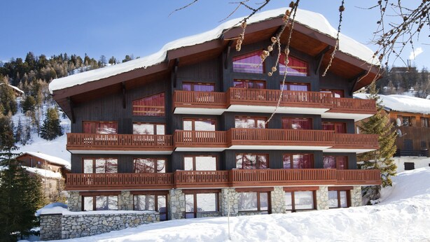 A multi-story chalet with wooden balconies, stone foundation, and a snow-covered roof. - VVF Résidence Plagne 1800 Paradiski (La Plagne-Tarentaise)
