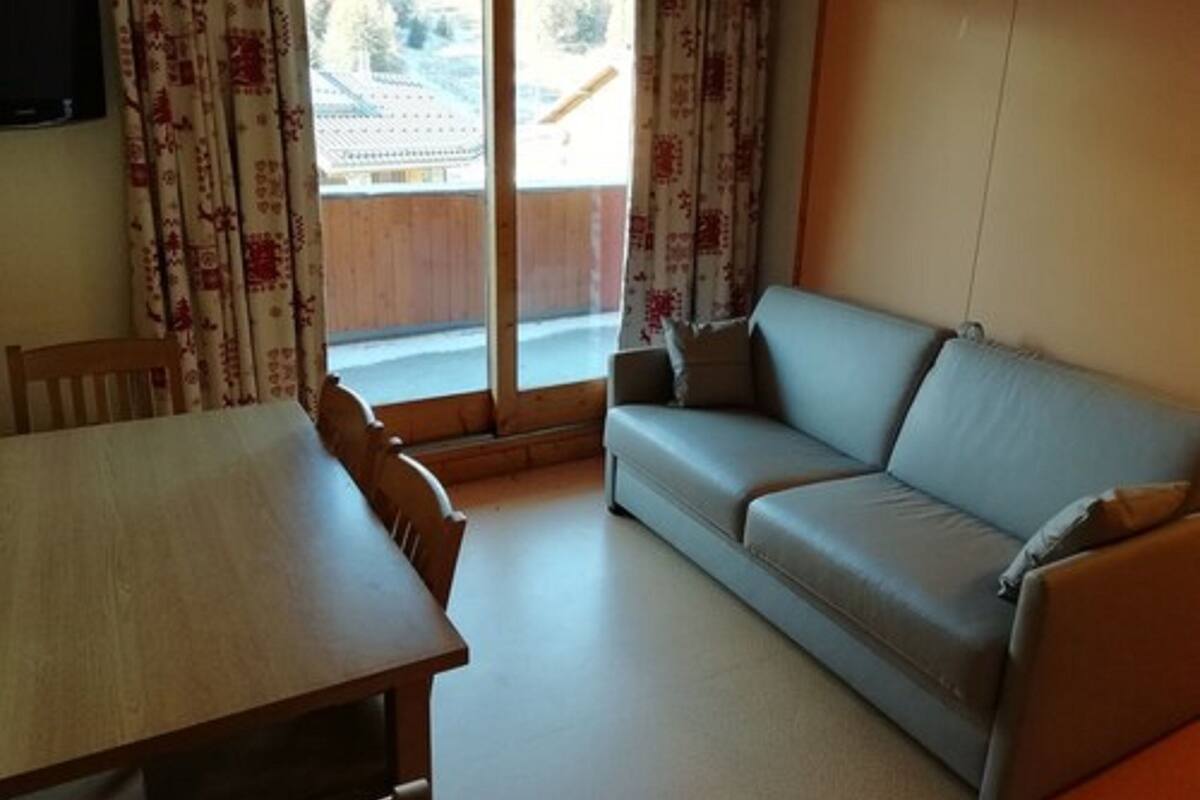 Una habitación con una mesa de comedor de madera, un sofá gris y un ventanal corredizo que da a un espacio exterior.