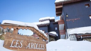 A wooden sign with "LES AROLES" in white letters, a snow-covered building, and a clear blue sky. - VVF Résidence Plagne 1800 Paradiski (La Plagne-Tarentaise)