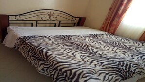 Ein Bett mit einem zebra-gemusterten Überwurf, einem Metall-Kopfstück und einem Fenster mit Vorhängen.