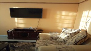 Ein Wohnzimmer mit einem an der Wand montierten Flachbildfernseher, einer Holz-Unterhaltungseinheit und einem gemusterten Sofa mit vielen Kissen.