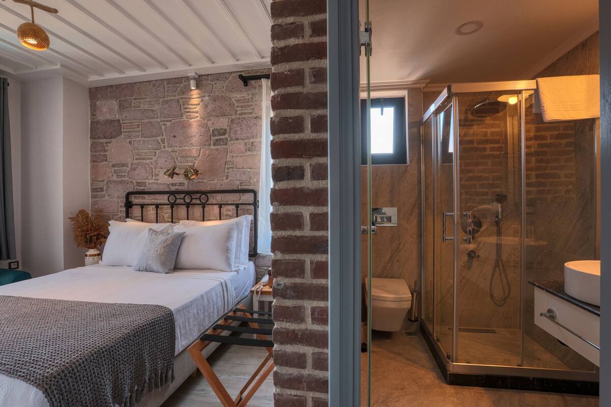 Ein Schlafzimmer mit einem Bett, einem Nachttisch, einer Nische für Nachttischutensilien, einer Ziegelwand und einer Duschkabine aus Glas.