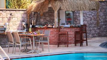 Een buitengebied met een bar, rieten dak, zwembad en een stenen muur.