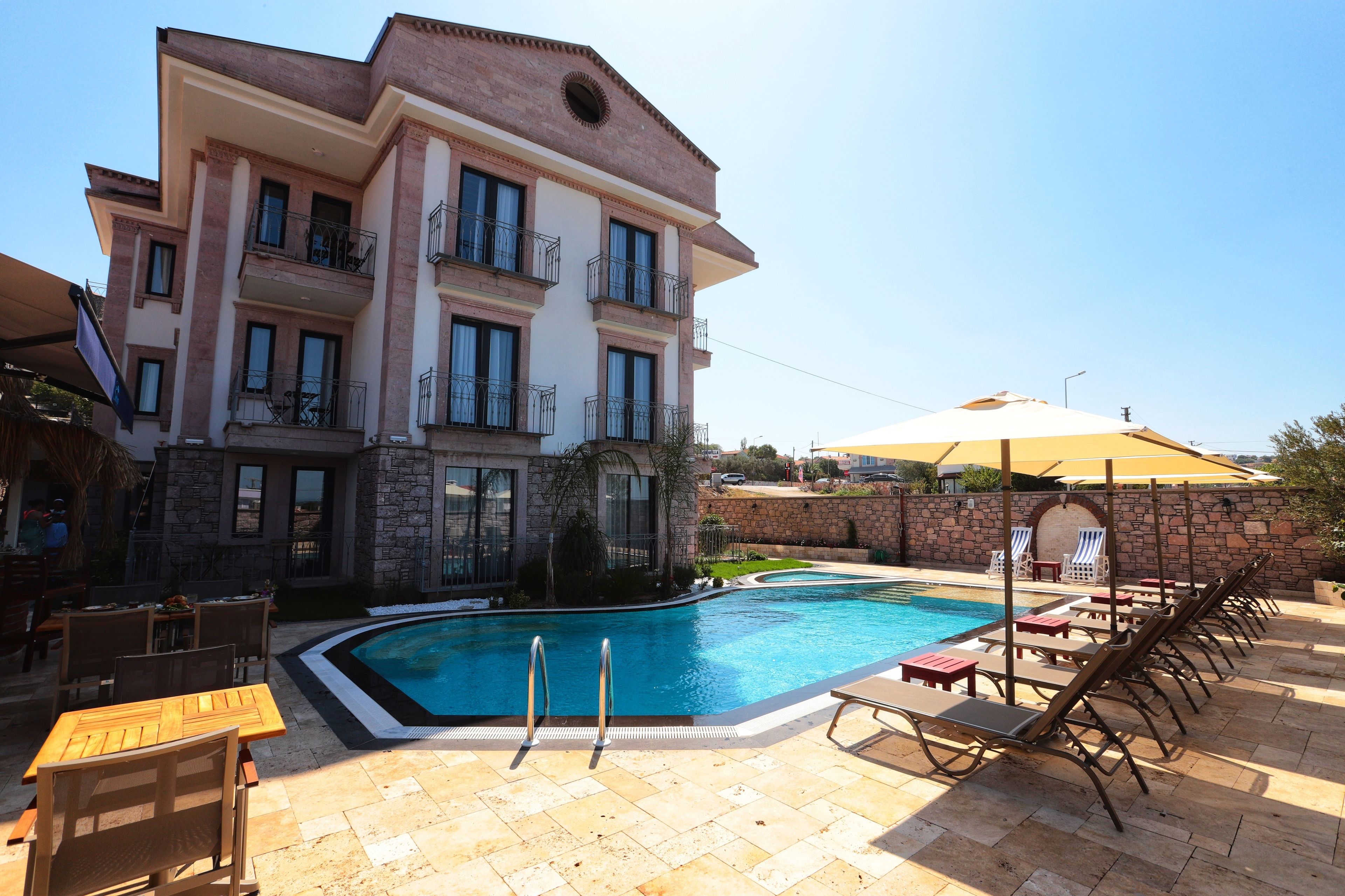 A large building with a swimming pool, outdoor seating, and a stone wall.