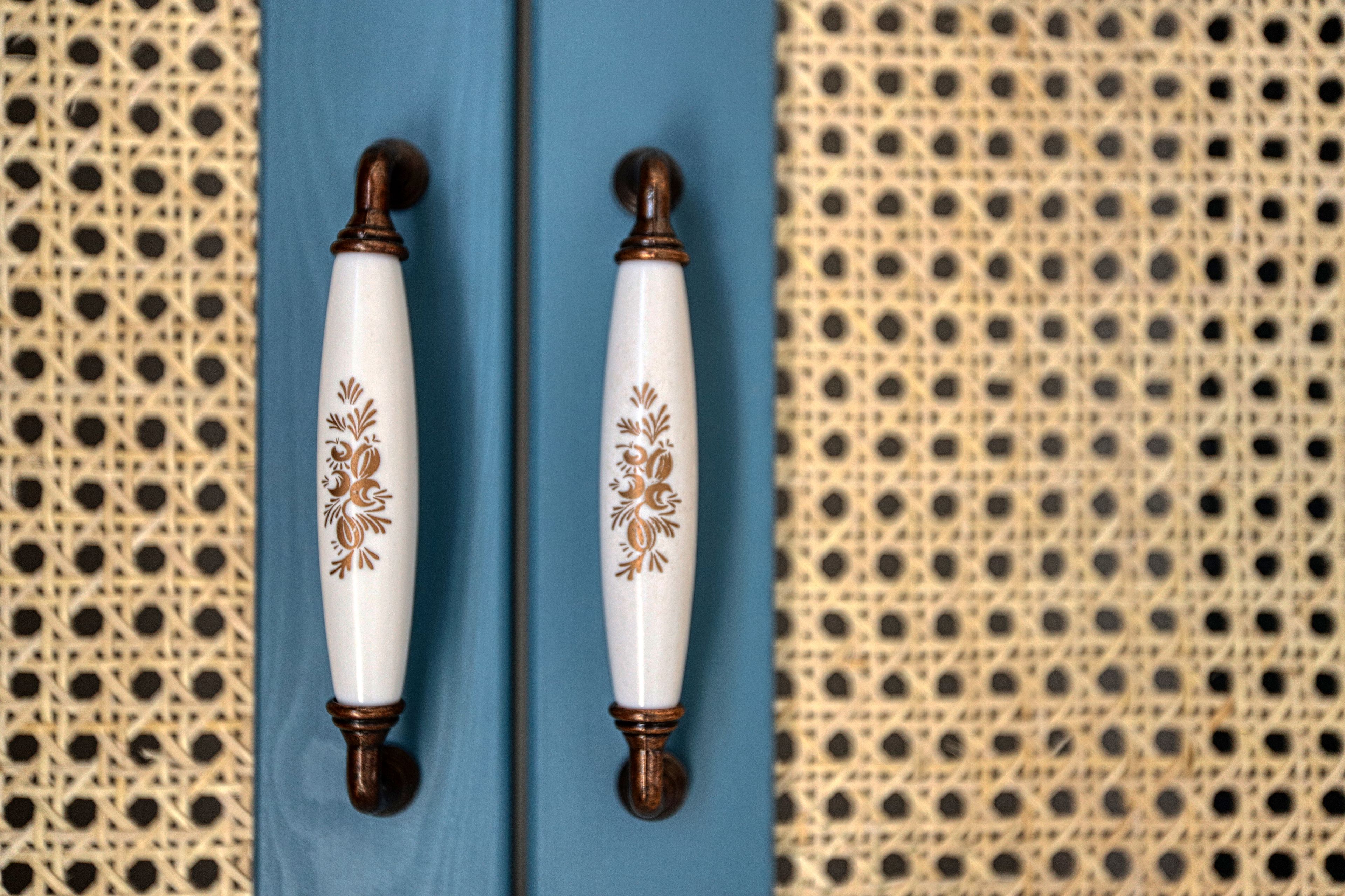 Deux poignées de porte blanches, agrémentées de motifs floraux et de touches de couleur marron, fixées sur une porte bleue.