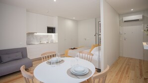 Ein moderner, gut beleuchteter Raum mit Esstisch für zwei Personen, einer Couch und einem Bett.
