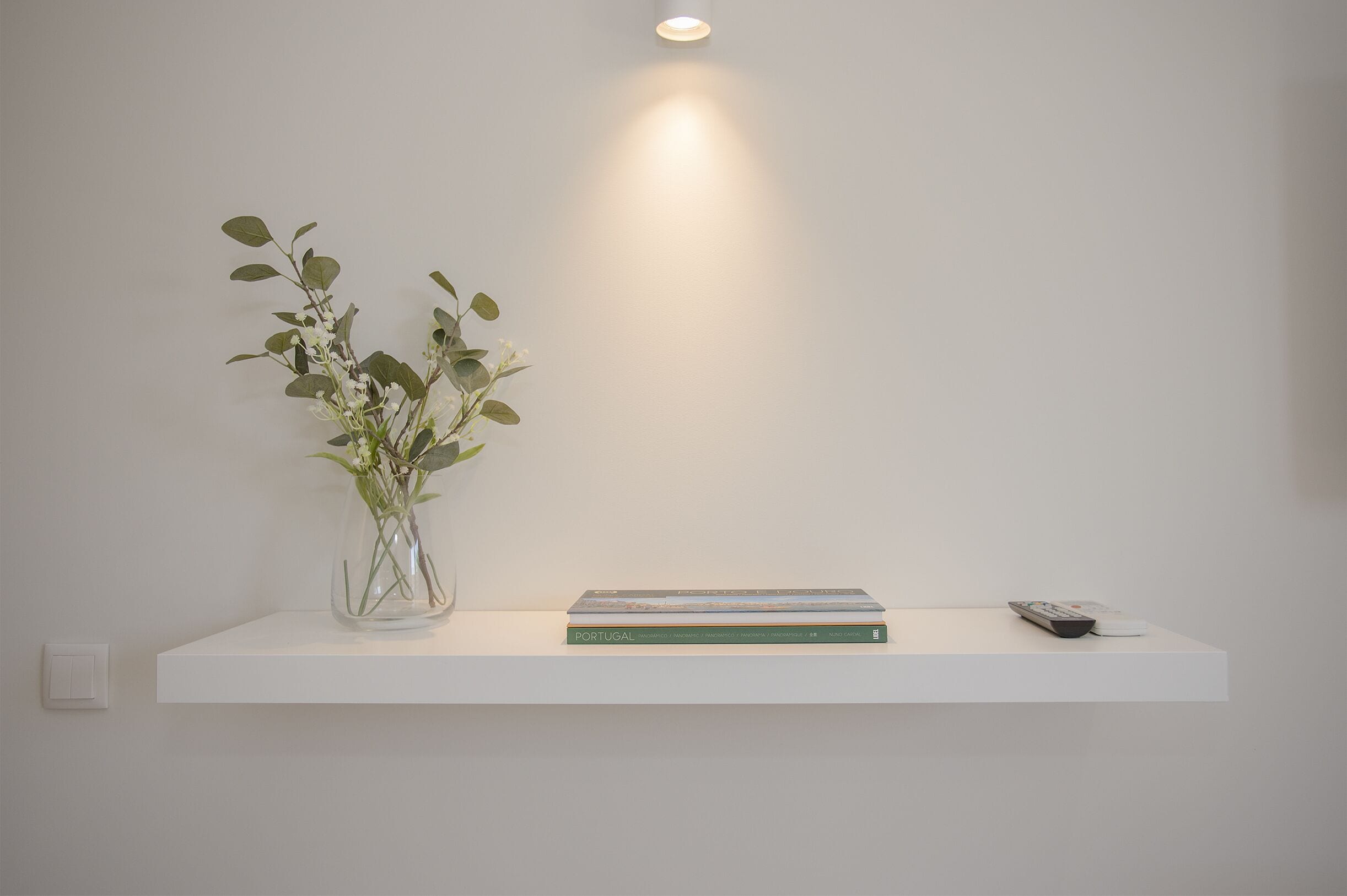 A white shelf with a vase of green plants, a book titled 'PORTUGAL', and a remote control.
