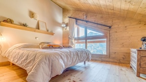 Ein gemütliches Schlafzimmer mit Holzbalkendecke, einem Bett mit weißer Bettdecke, einem Nachttisch und einem Fenster mit Bergblick.