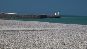 Une plage de galets avec un phare et une jetée qui s’avance dans la mer.