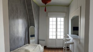 Une chambre à coucher avec un lit, un miroir, une fenêtre et un radiateur.