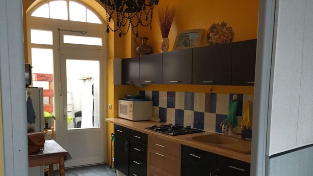 Une cuisine équipée d’un four à micro-ondes, d’une cuisinière et de placards. Il y a une fenêtre avec des rideaux et une porte qui donne sur une autre pièce.