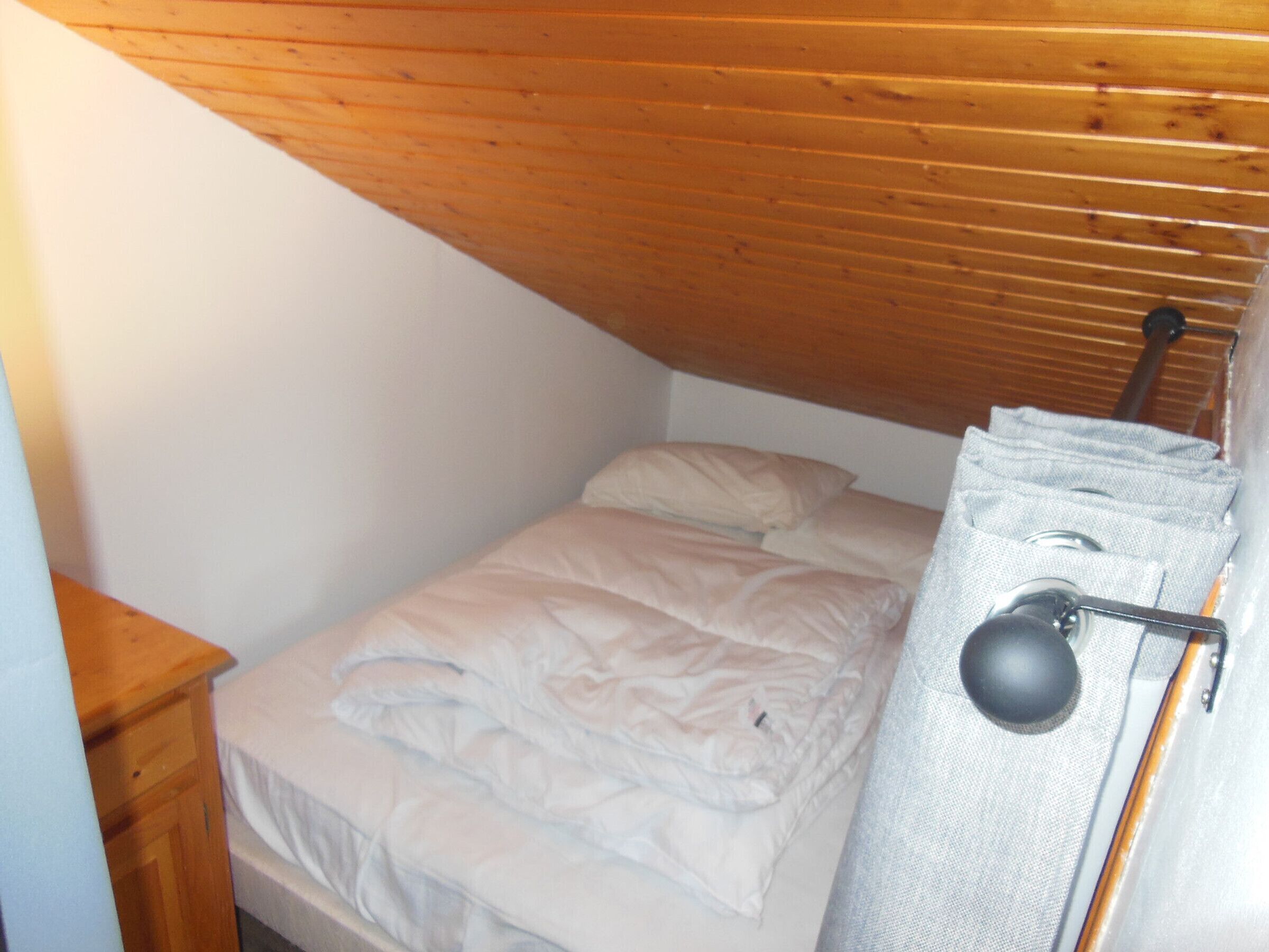 A small, single-bed room with a wooden ceiling and a white wall.