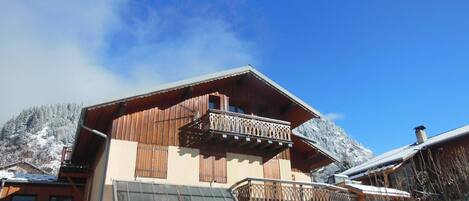 A chalet with a stone facade, wooden balconies, and a view of snow-covered mountains.