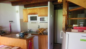 A compact kitchen with wooden cabinets, a microwave, a refrigerator, and a dining area with a table and chairs. - Champagny-en-Vanoise: 5-room apartment, 8 pers, pets allowed (Champagny-en-Vanoise)