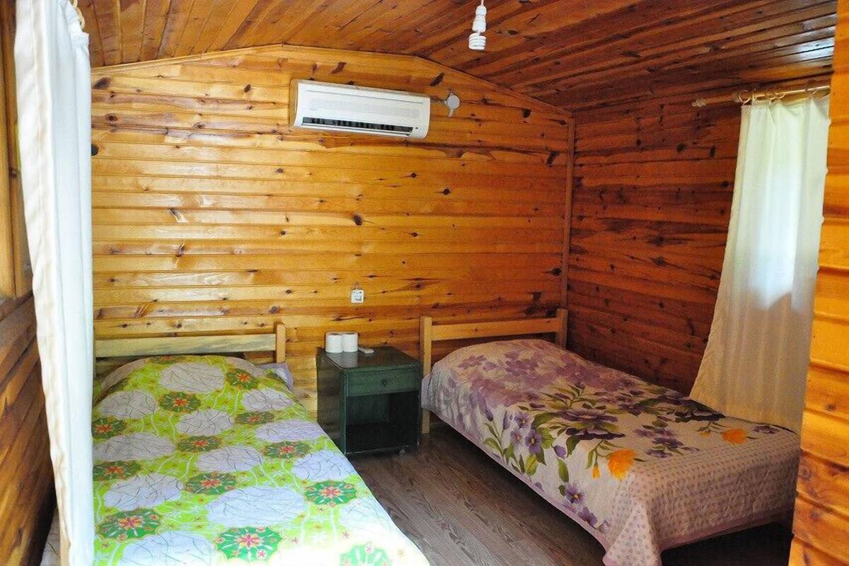 Ein kleines Zimmer in einer Holzhütte mit zwei Betten, einer Klimaanlage und einem Nachttisch.