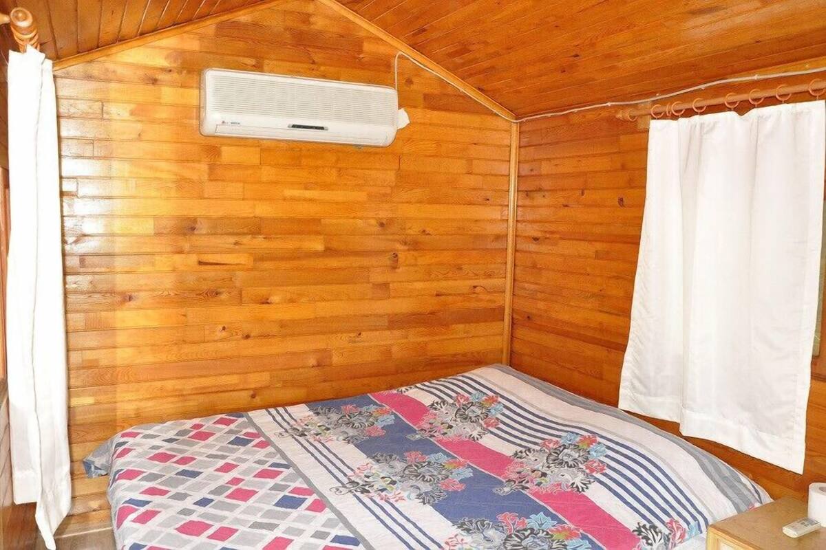 Ein Zimmer mit Holzwänden, einem Bett, einer weißen Klimaanlage und einem Vorhang.