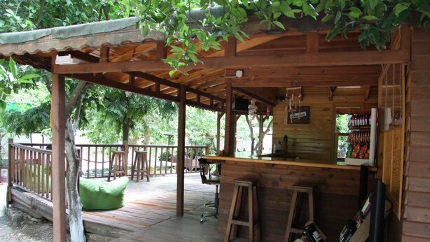 A wooden outdoor bar area with a wooden deck, a green cushioned seating area, and a wooden railing. - Olympos Alaturka Pansiyon (Kumluca)