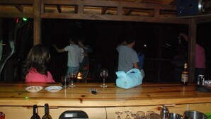 A bar area with wooden beams, bottles, glasses, and a blue bag on the counter. - Olympos Alaturka Pansiyon (Kumluca)